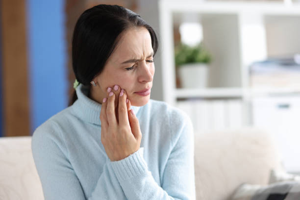 A woman wearing a blue sweater grasps her jaw in pain.