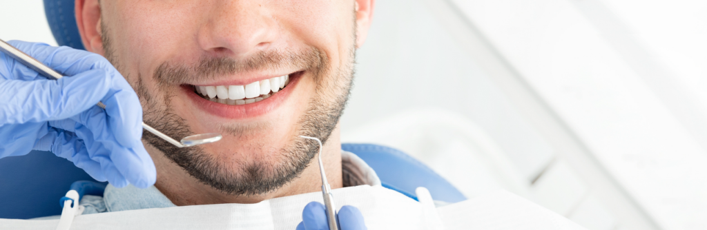 The lower half of the face of a smiling young man receiving dental care.