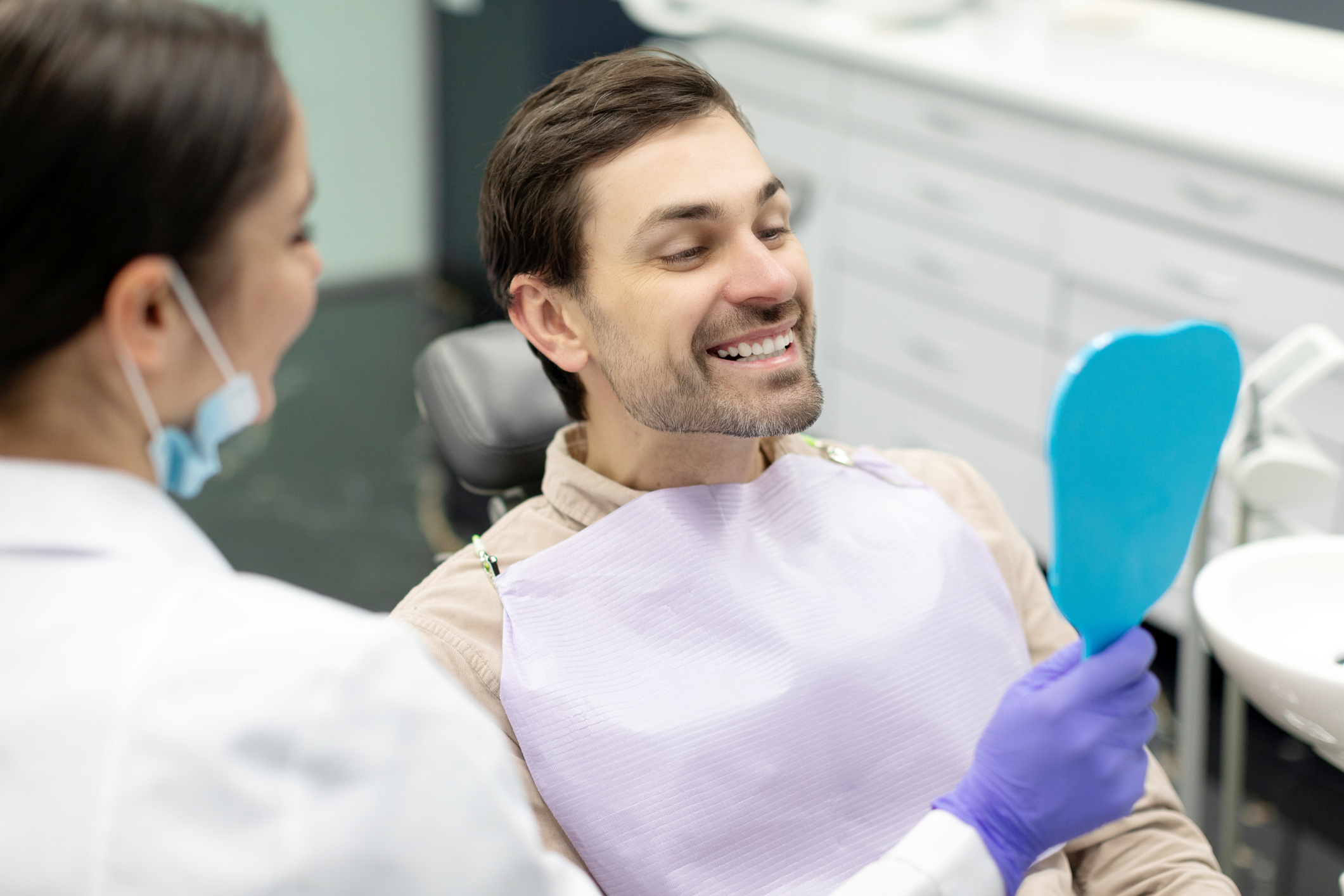 Man smiling in mirror deciding on veneers or implants