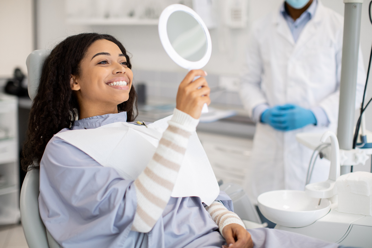 Patient smiling while viewing her teeth in a mirror during a cosmetic dentistry appointment.